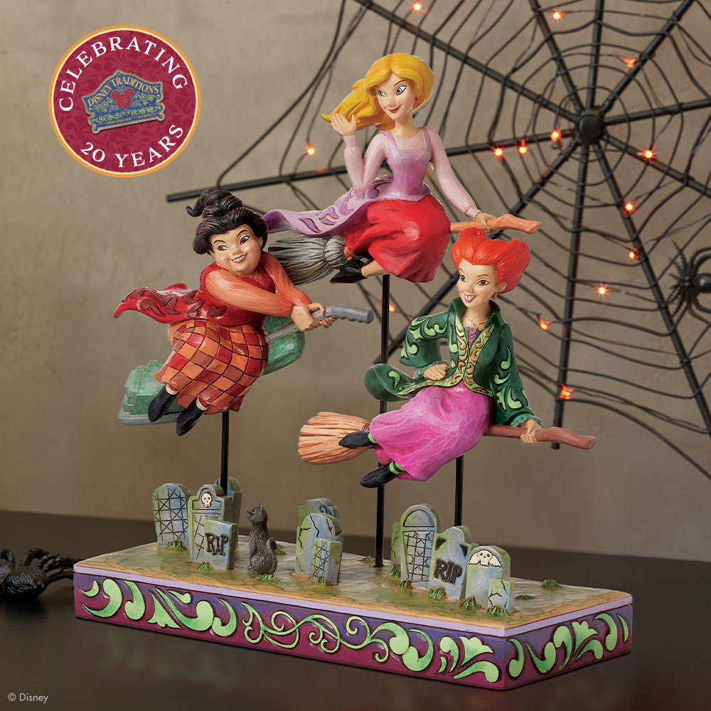 Three witch figurines on brooms with a spider web and 'Celebrating 20 Years' logo in the corner.