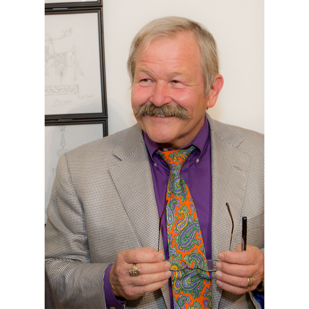 Jim Shore wearing a colorful paisley tie and gray suit jacket indoors.