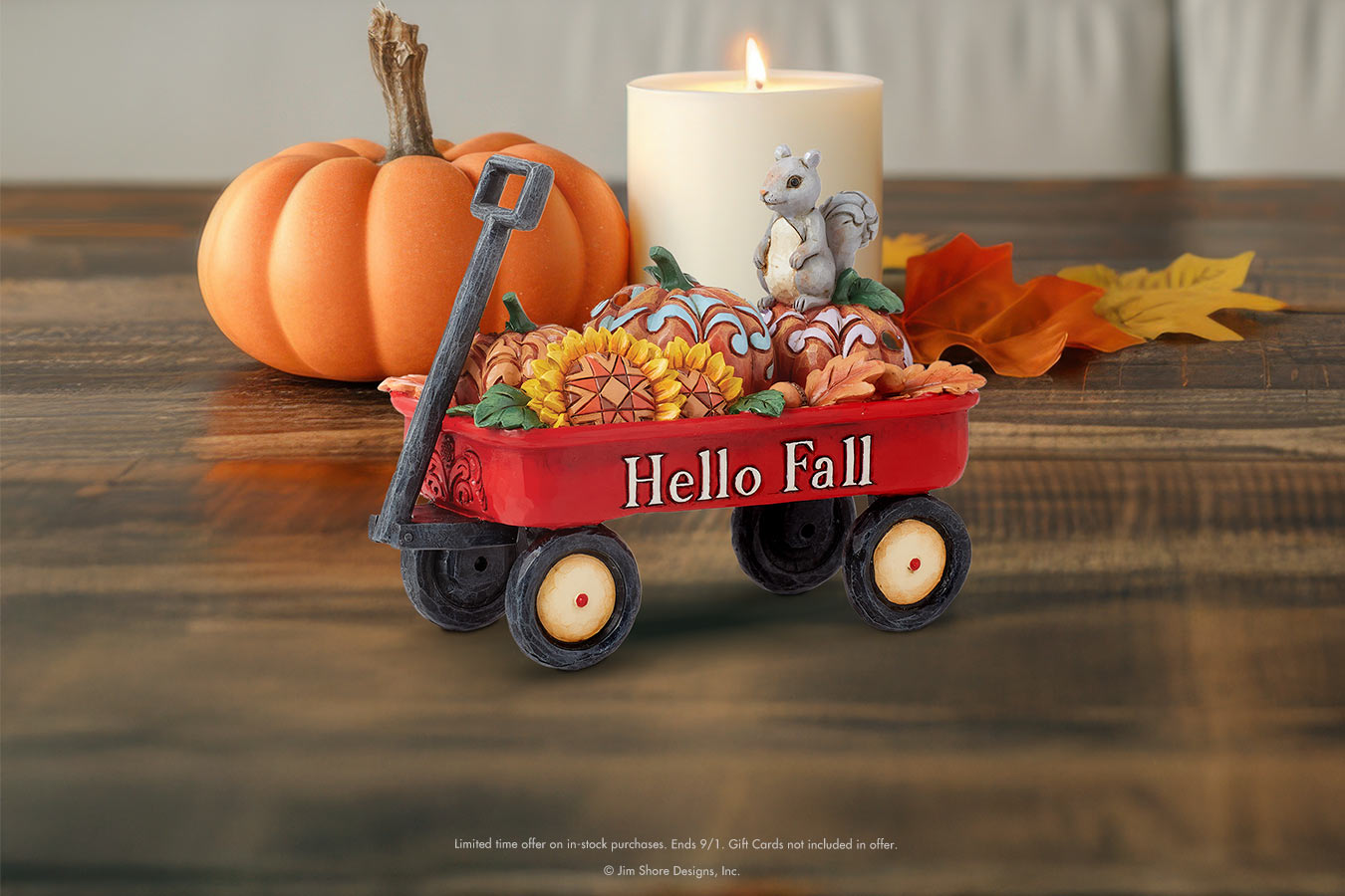 Decorative red wagon with 'Hello Fall' text, pumpkins, and candle on a wooden surface.