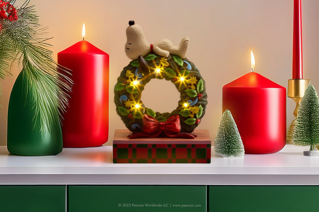 Decorative Christmas scene with candles, a wreath, and small trees on a shelf.