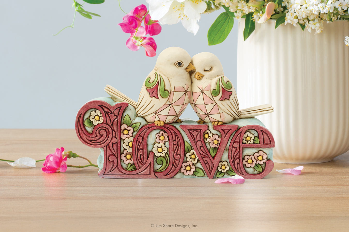 Decorative piece with two birds on a 'LOVE' sign, surrounded by flowers on a wooden surface.