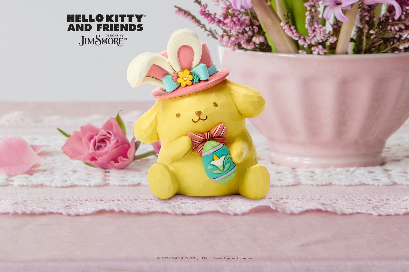 Yellow character figurine with bunny ears and a pink hat on a pink surface with flowers.