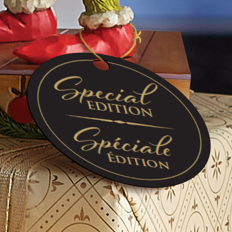 A black oval hanging tag with gold lettering reading 'Special EDITION' and 'Spéciale Édition' on a gift box, with red decorative ornaments in the background.