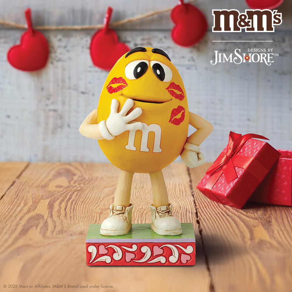 M&M's figurine with red lipstick marks on a wooden surface, featuring Jim Shore branding.