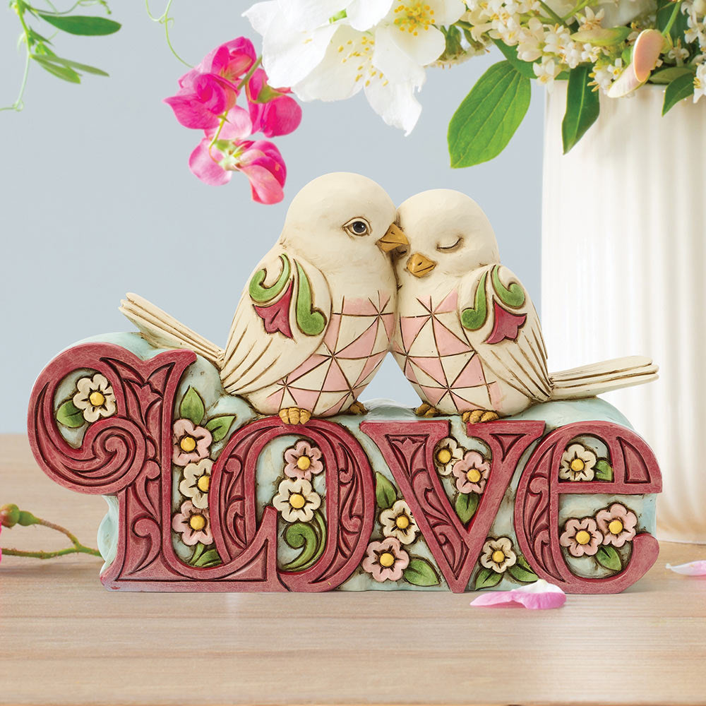 Decorative figurine of two birds on a 'LOVE' sign with flowers in the background